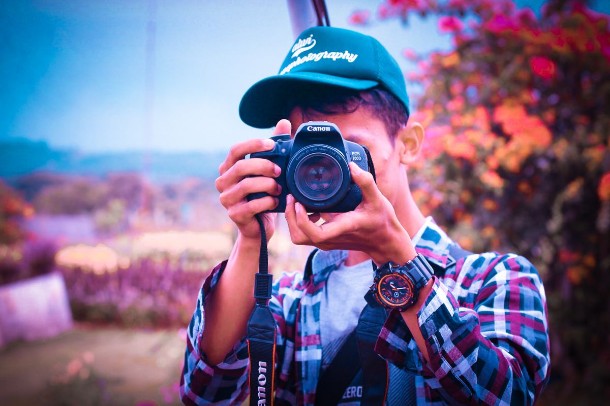 Een jonge mannelijke fotograaf in Ciawi, Indonesië, die buiten foto's maakt met een DSLR-camera.