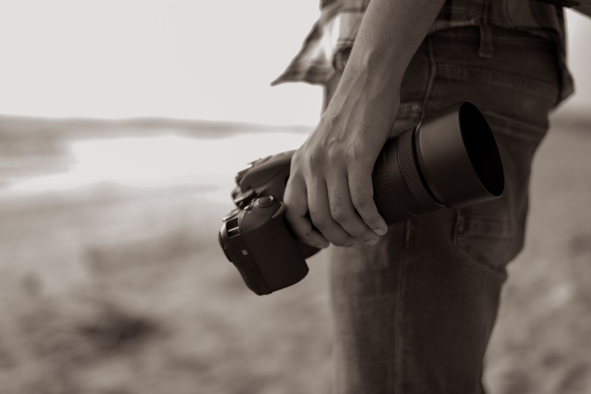 Een close-up afbeelding van een persoon die een camera vasthoudt op het strand, wat een serene sfeer uitstraalt.