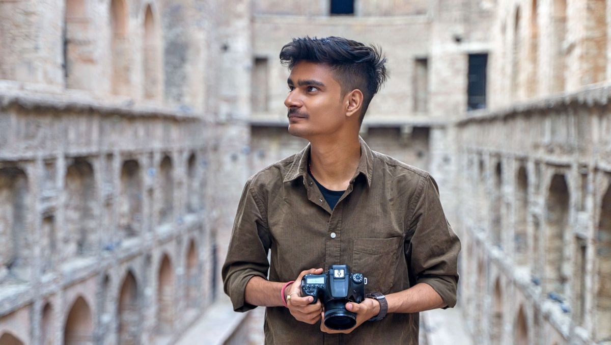 Een jonge man met een camera in een historische architecturale omgeving buiten.