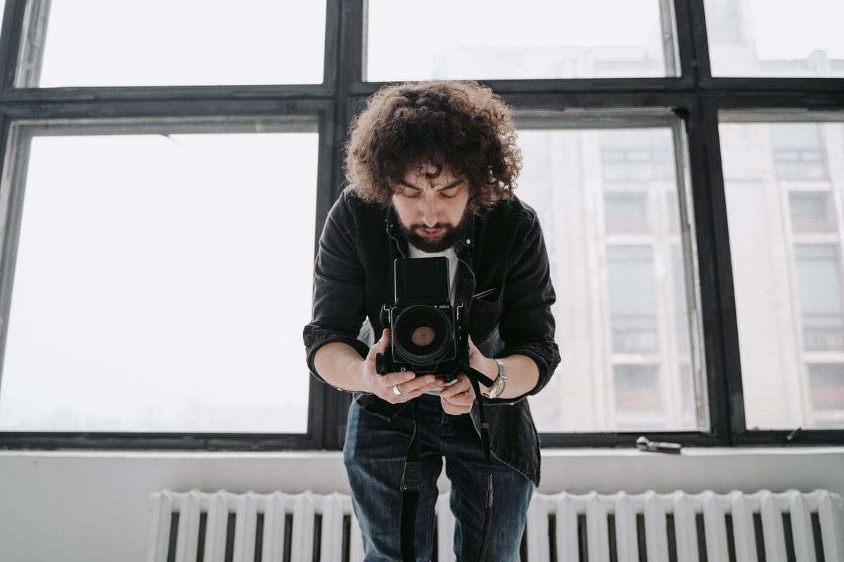Fotograaf die binnen een professionele camera gebruikt, zich richt op een studio met grote ramen.